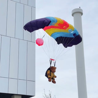 Teddy bear jumping from a building with  with a mini parachute toy.